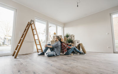 Couple sitting on floor of their new home among moving boxes