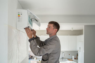 Man technician woker in uniform installing air conditioner in modern apartment.