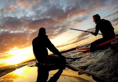 Silhouette people on boat against sea during sunset