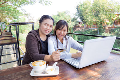 Smiling young woman using mobile phone while sitting on table