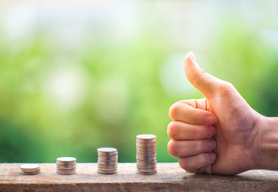 Cropped hand of person gesturing thumbs up by stacked coins outdoors