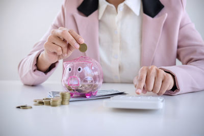 Midsection of businesswoman calculating coins while inserting in piggy bank