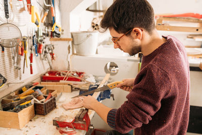 Side view high angle of busy male woodworker using sharp saw and cutting wooden plank in workshop