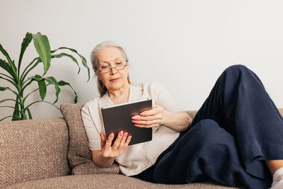 Portrait of young woman using digital tablet while sitting on sofa at home