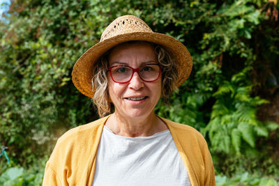 Positive middle aged female in casual clothes with glasses and sunhat smiling and looking at camera during work on farm in highland