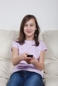 Portrait of smiling young woman holding remote control while sitting on sofa at home