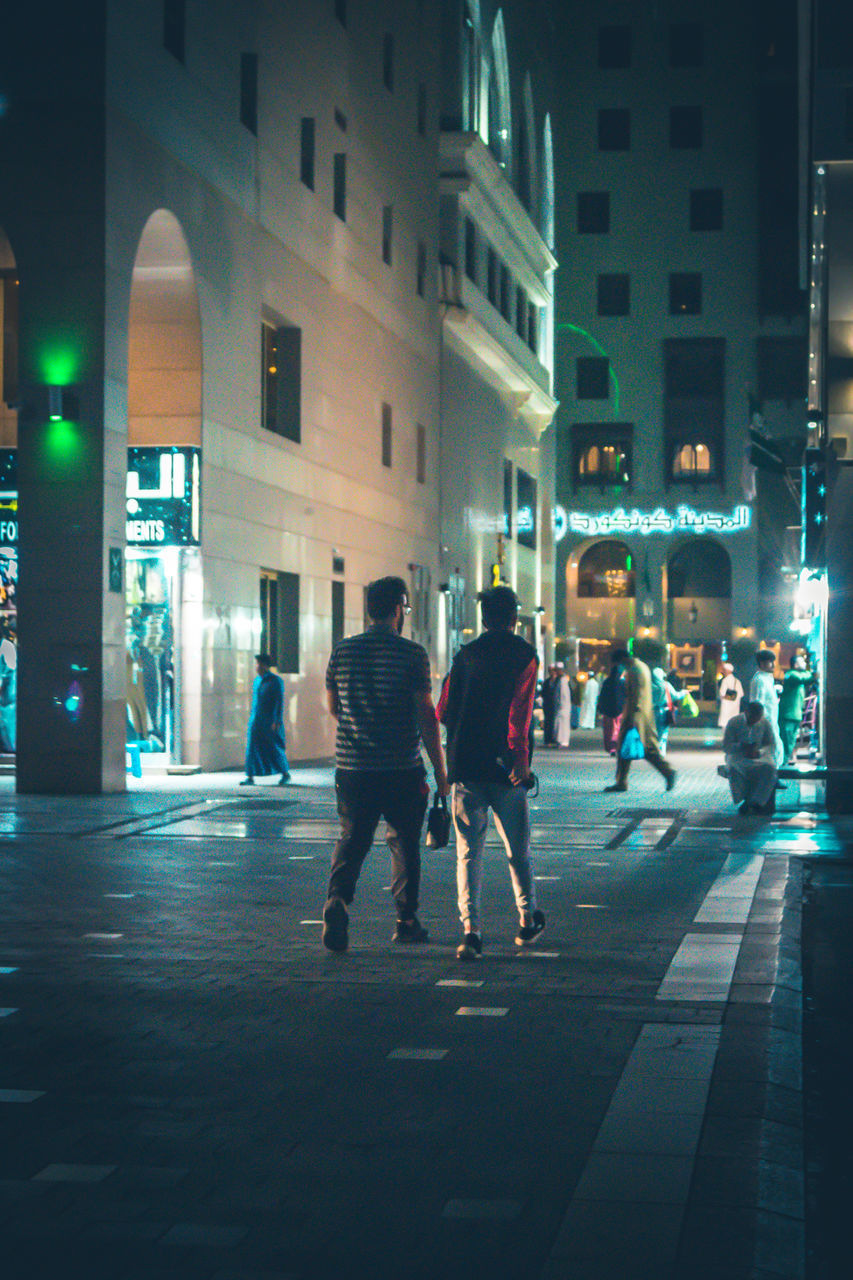 PEOPLE WALKING ON STREET AGAINST ILLUMINATED BUILDINGS AT NIGHT