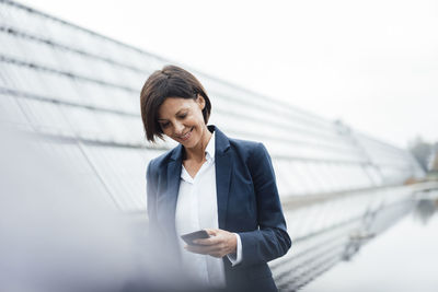 Smiling businesswoman text messaging on smart phone outside office building