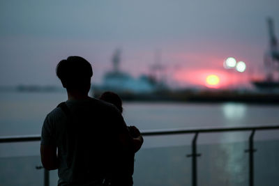 Rear view of silhouette father with son at harbor against sky during sunset