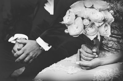 Midsection of bride holding bouquet while sitting by groom