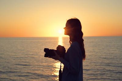 Woman standing by sea against sky during sunset