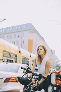 Young businesswoman locking bicycle on road in city against sky