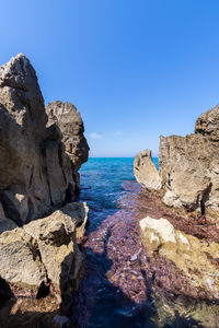 Rocks on sea shore against clear blue sky