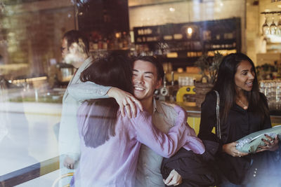 Man embracing female friend seen through glass of restaurant