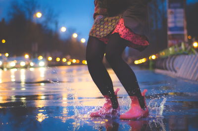 Low section of woman splashing water on street during rainy season