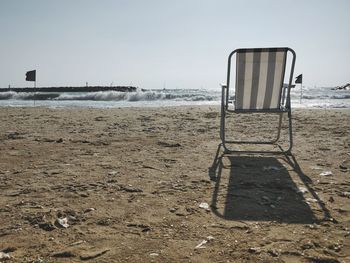 Chair on beach against clear sky