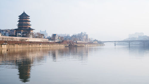 View of buildings by river against sky in city