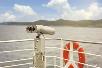 Close-up of coin-operated binoculars by sea against sky