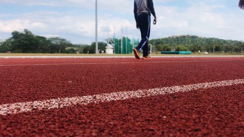 Low section of man walking on running track against sky