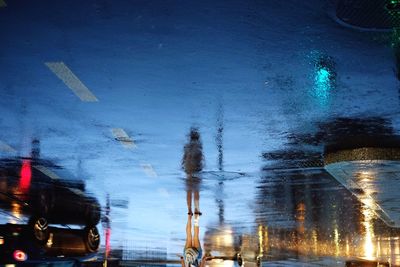 Upside down image of woman reflection on wet street at dusk during monsoon