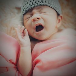 Close-up of cute baby girl yawning on bed