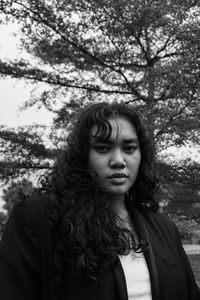 Portrait of young woman standing against trees