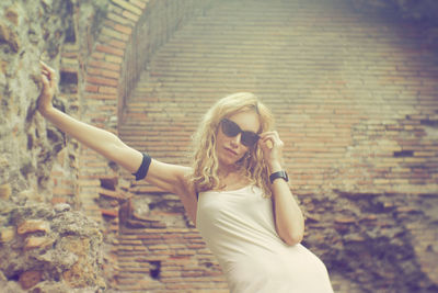 Portrait of woman in sunglasses standing against brick wall