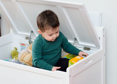 Little toddler playing with his plush toys inside the toy box