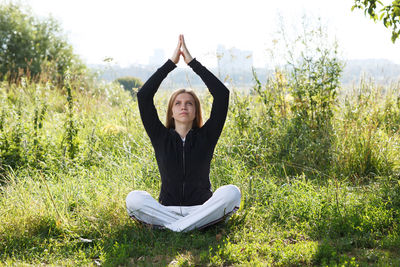 Young woman exercising while sitting on field 