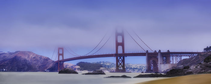 Suspension bridge over sea against cloudy sky