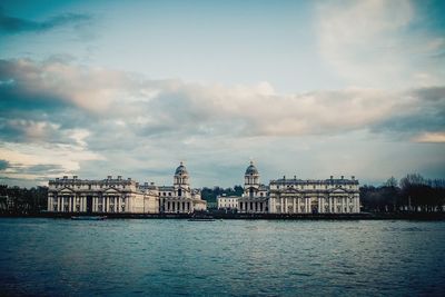 Buildings at waterfront against cloudy sky