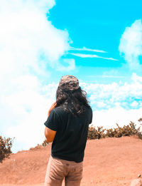 Rear view of woman standing on rock against sky