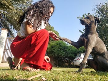 Side view of woman holding dog paw on grassy field