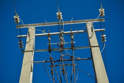 Low angle view of electricity pylon against clear blue sky