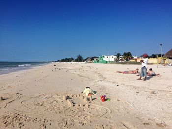 People relaxing on beach against clear sky