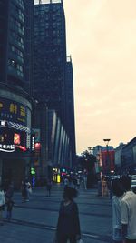 People walking on street by modern buildings in city against sky