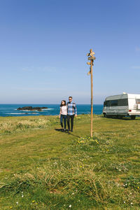 Couple standing on field by sea against sky
