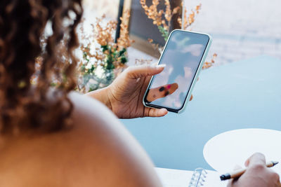 Unrecognizable african american female sitting at table in cafe and chatting on social media while relaxing during weekend in city