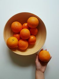 Close-up of hand holding orange fruit against white background