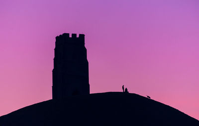 Silhouette tower church and  person standing by pink against sky during sunset