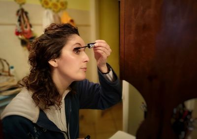 Mature woman applying mascara at home