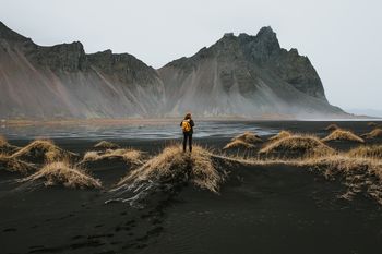 REAR VIEW OF WOMAN STANDING ON ROCK AGAINST MOUNTAINS