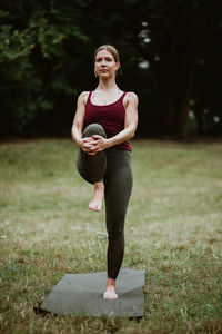 Full length portrait of woman stretching on field and yoga mat