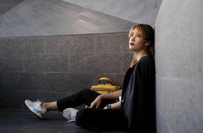 Side view of thoughtful businesswoman looking away while sitting by wall