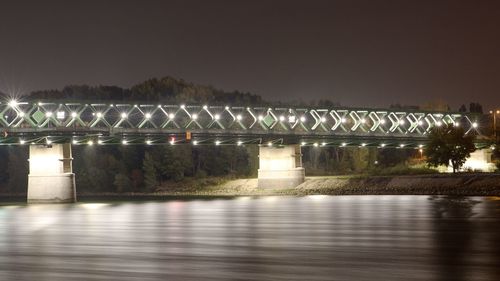Illuminated bridge over river against sky at night