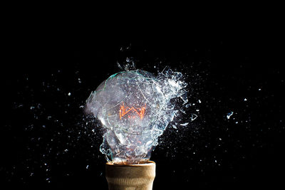 Close-up of light bulb breaking against black background