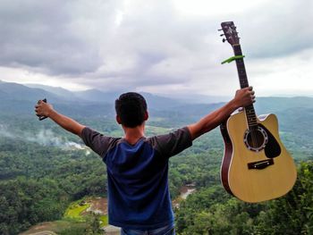 Rear view of man playing guitar against sky