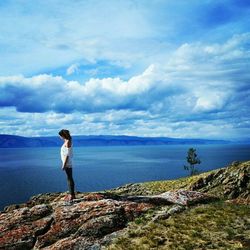 Woman standing on rock by lake against sky