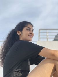 Side view of young woman looking away against sky