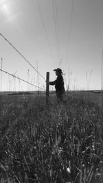 Side view of man standing by fence on land against sky